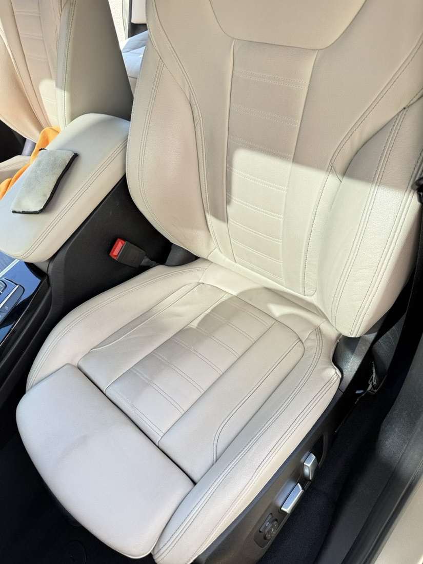 Leather seat photographed mid-clean — one half scrubbed, the other still soiled